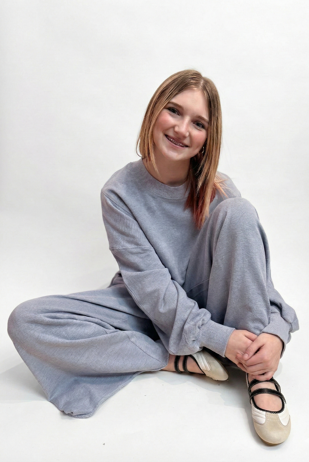 Person wearing a gray outfit sitting on a white background