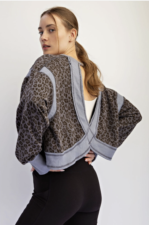 A woman modeling a cropped leopard-print jacket with light gray contrast panels and a wrap-style back, shown against a plain light gray studio background.