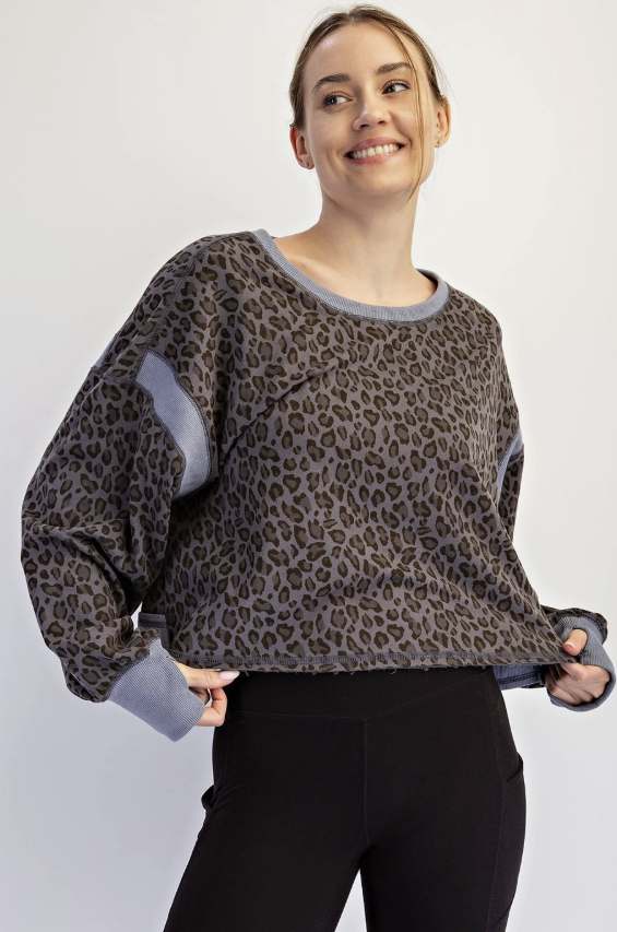 A woman wearing a gray and black leopard-print long-sleeve top with solid gray ribbed trim and solid gray elbow patches, paired with black leggings, against a light gray studio background.