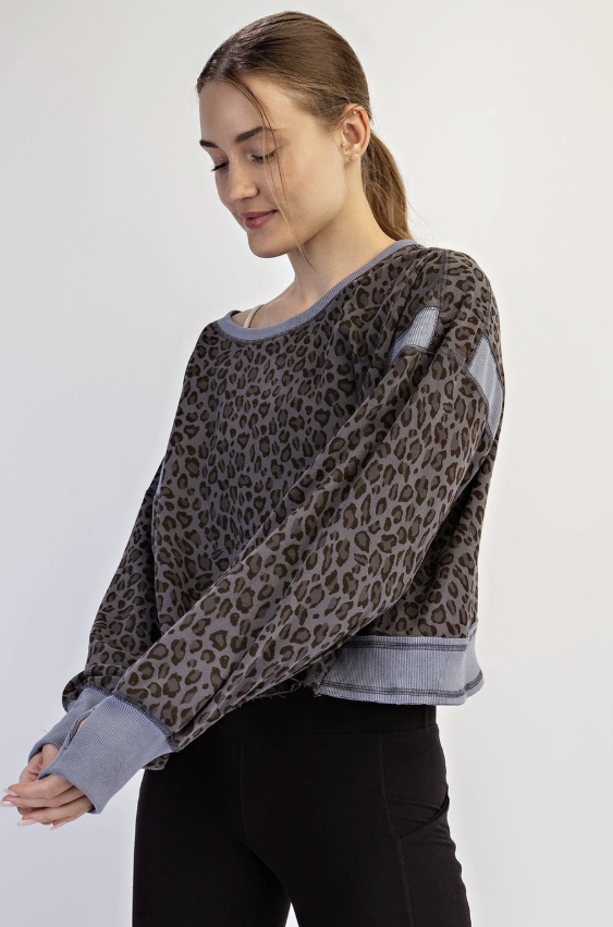 A woman wearing a cropped long-sleeve top with a brown and gray leopard print pattern and contrasting gray ribbed trim, paired with black pants, against a plain light gray background.