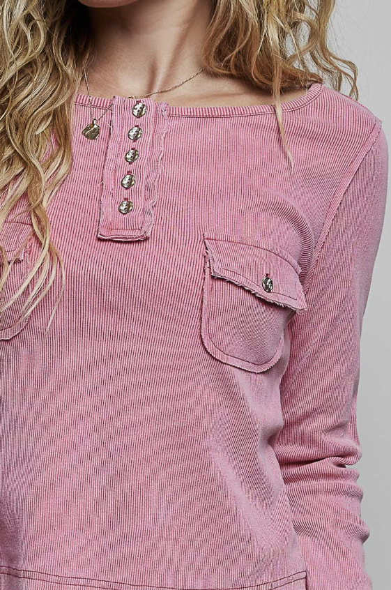 A close-up of a woman wearing a pink ribbed long-sleeve henley top with decorative metal buttons and a chest pocket.