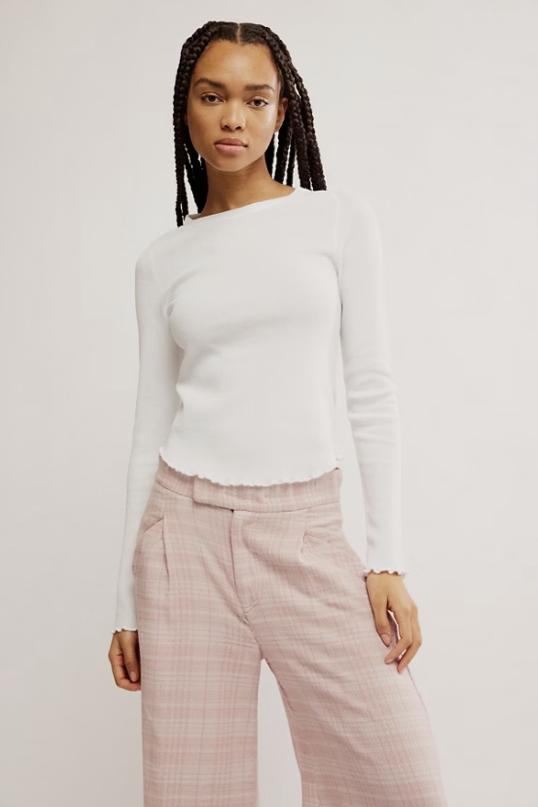 Woman wearing a white sweater and pink checkered pants against a plain background