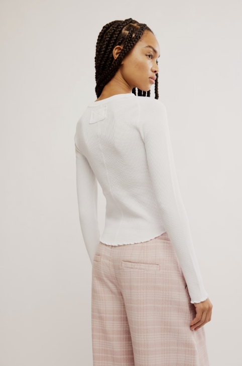 Person wearing a white long-sleeve top and pink plaid pants on a plain background