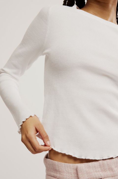 Close-up of a person wearing a white ribbed long-sleeve top with a blurred background