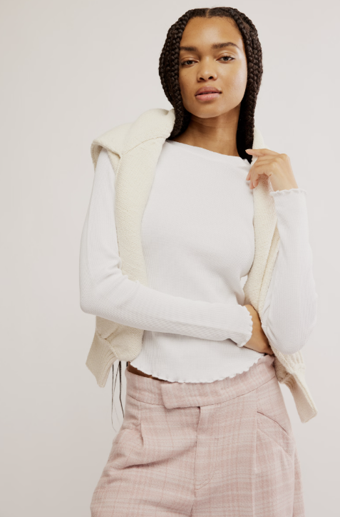 Woman wearing a white sweater and beige jacket against a plain background
