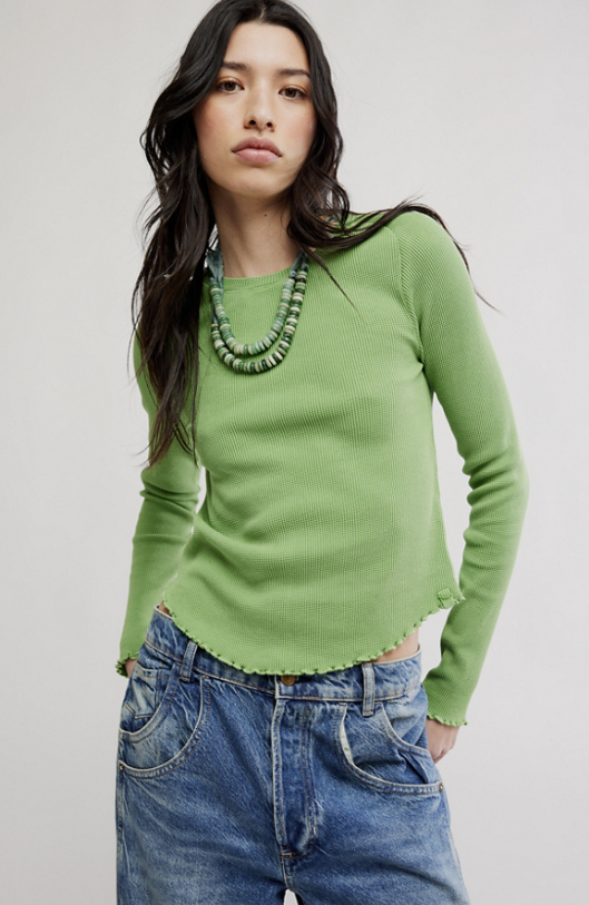 Woman wearing a green sweater and blue jeans against a plain background