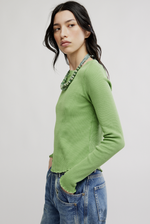 Woman wearing a green sweater and blue jeans against a plain background