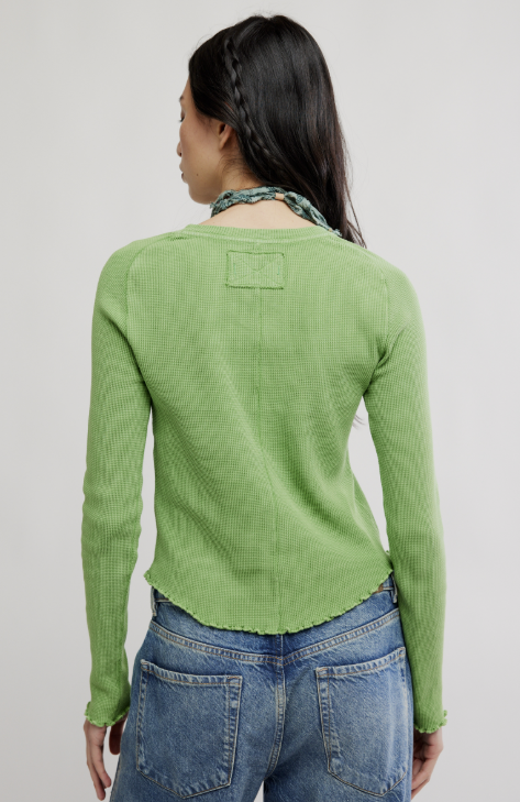 Person wearing a green ribbed sweater and blue jeans on a plain background