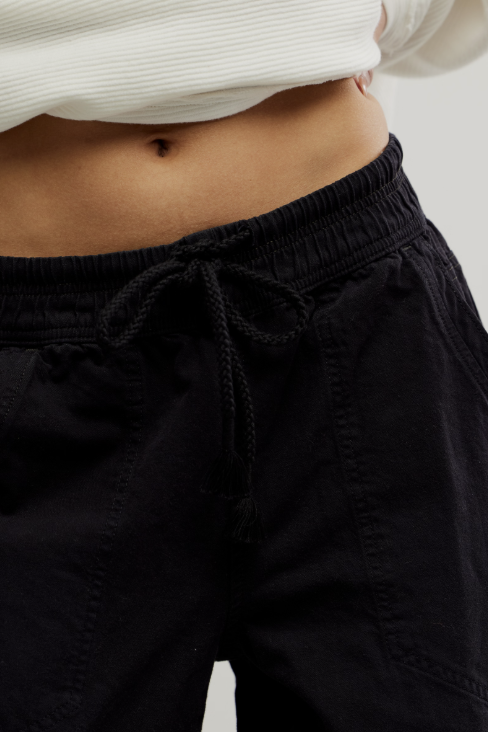Close-up of a person wearing black drawstring pants with an elastic waistband, paired with a white ribbed cropped top.