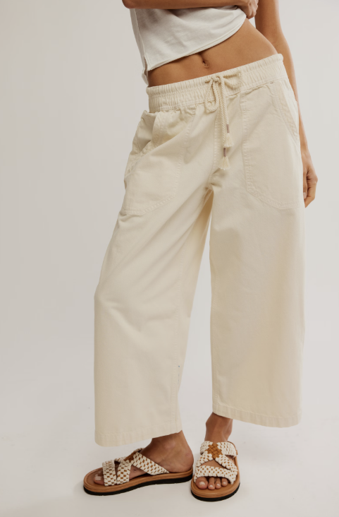 A person wearing off-white cropped wide-leg pants with a drawstring waistband, paired with woven slide sandals, shown against a plain light background.