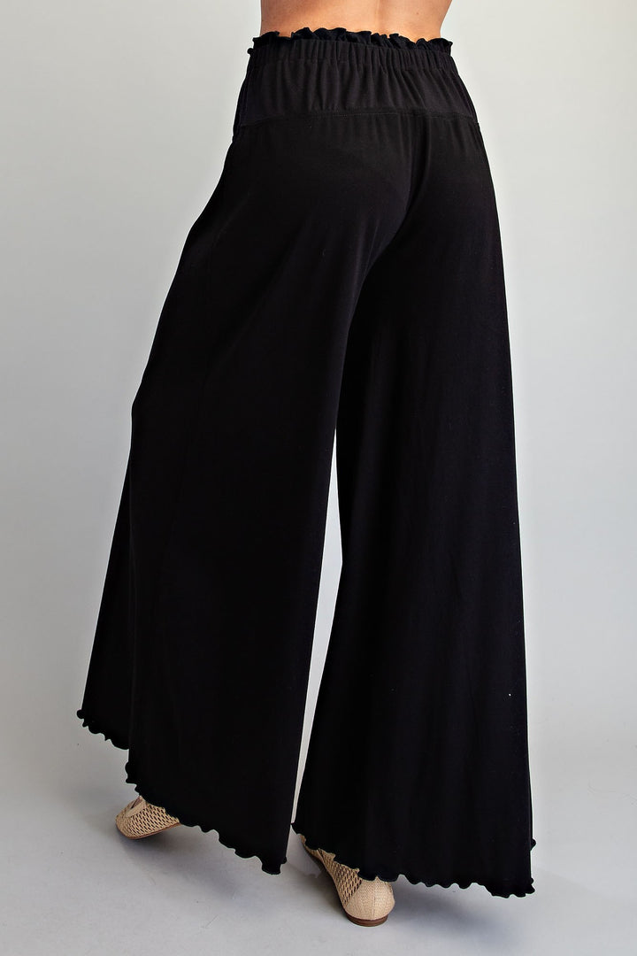 Black wide-leg pants with an elastic waistband and scalloped hem, shown on a model from the back against a light gray studio background.