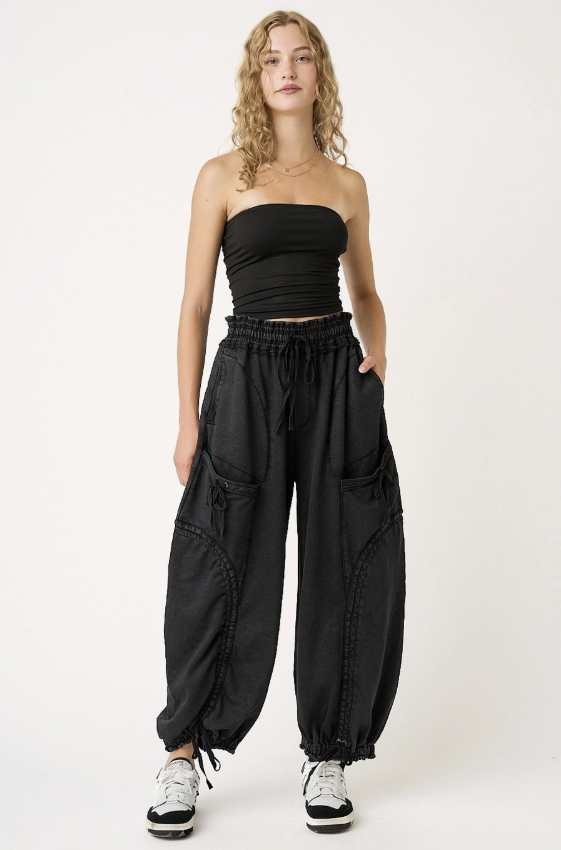 A model wearing a black strapless tube top and black wide-leg cargo pants with drawstrings, paired with white sneakers, against a plain white studio background.