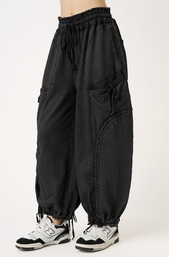 Black baggy jogger-style cargo pants with an elastic drawstring waist and elastic cuffs, shown on a model wearing white and black sneakers against a plain light background.