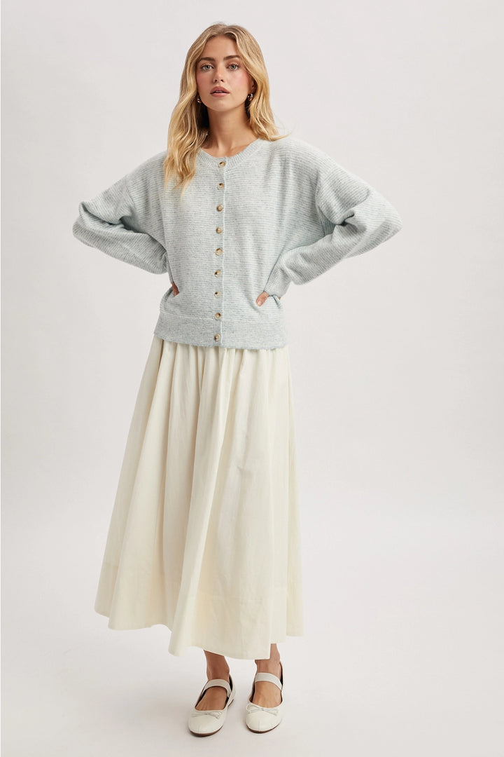 Woman wearing a mint cardigan over a long cream skirt on a white background