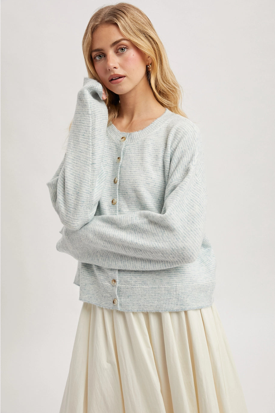 Woman wearing a mint cardigan over a cream dress on a white background