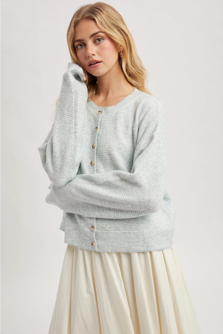 Woman wearing a mint cardigan over a cream dress on a white background