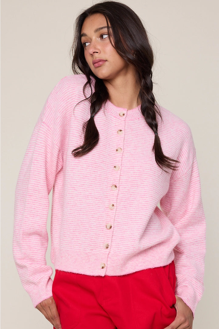 Woman wearing a pink cardigan with gold buttons against a plain background