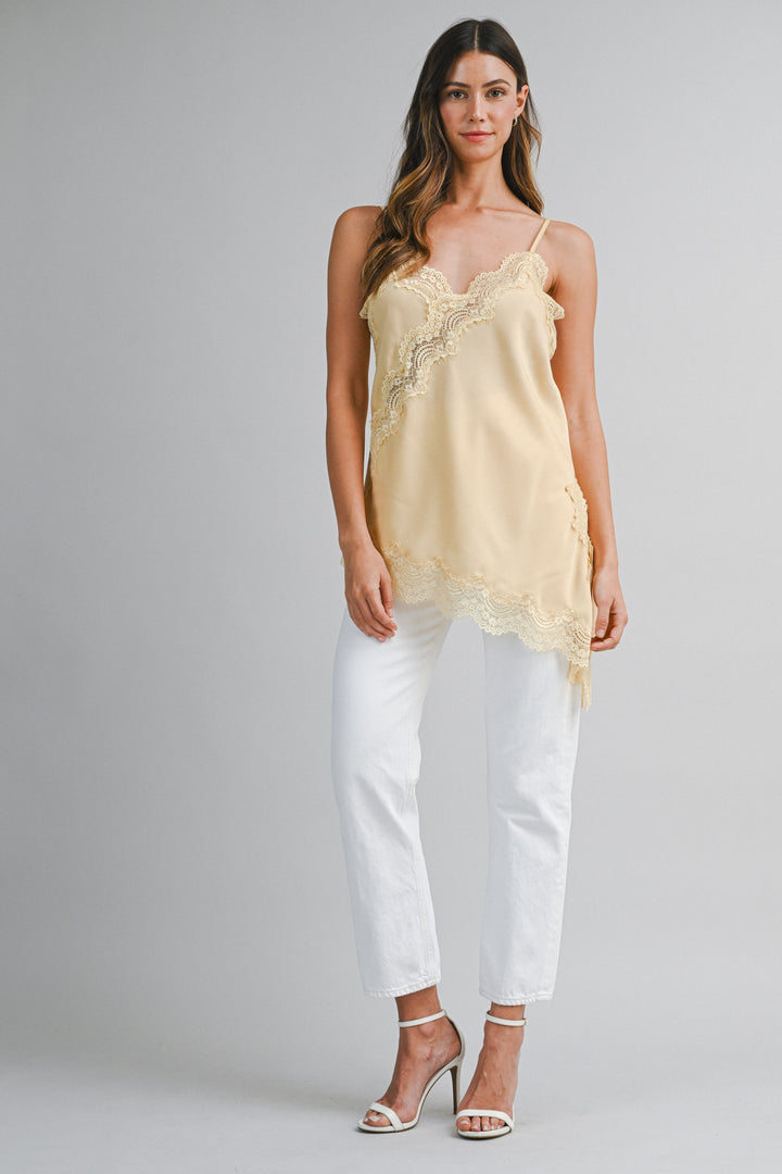 Woman wearing a light yellow lace top and white pants on a gray background