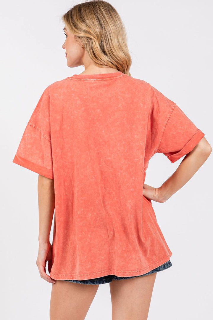 Back of woman wearing orange tee and denim shorts on plain background
