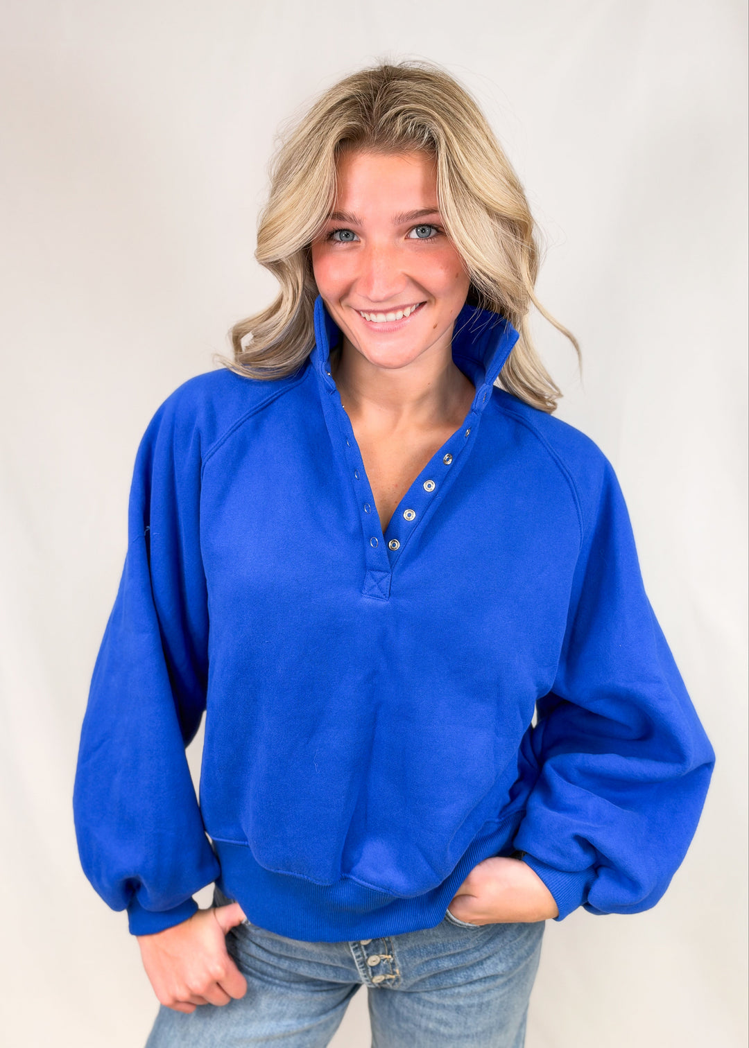 Woman wearing cobalt blue henley pullover with jeans on plain background
