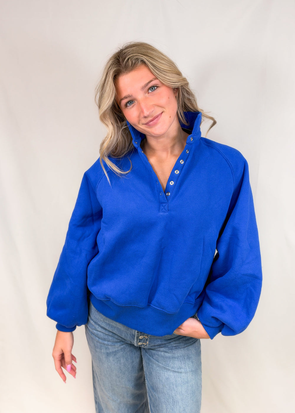Woman wearing cobalt blue henley pullover with jeans on plain background