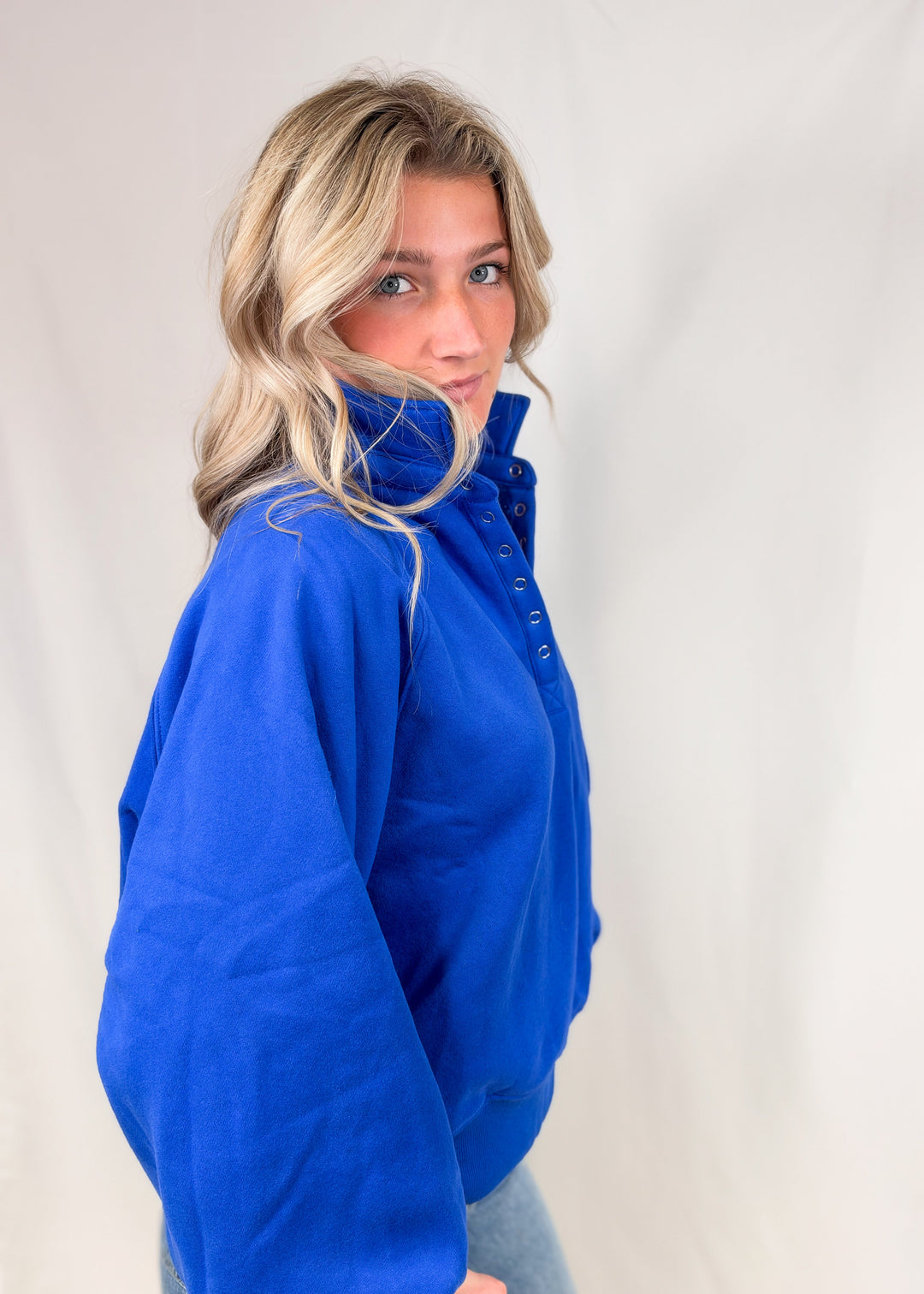 Woman wearing cobalt blue henley pullover with jeans on plain background