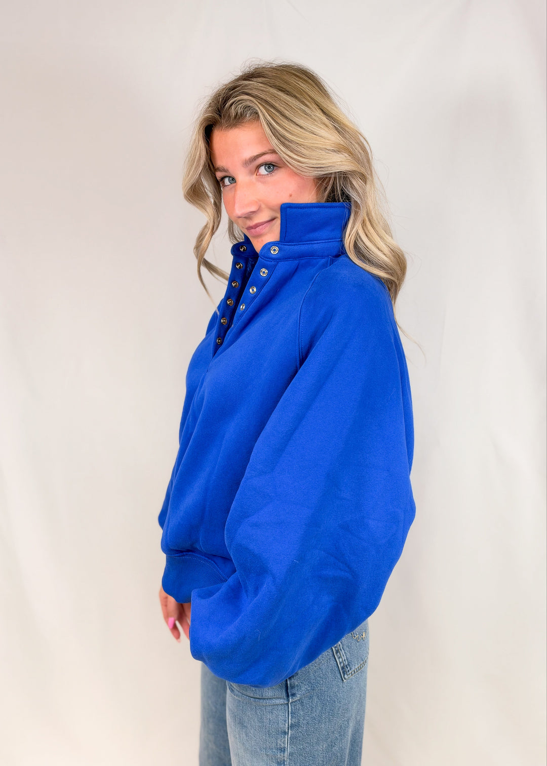 Woman wearing cobalt blue henley pullover with jeans on plain background