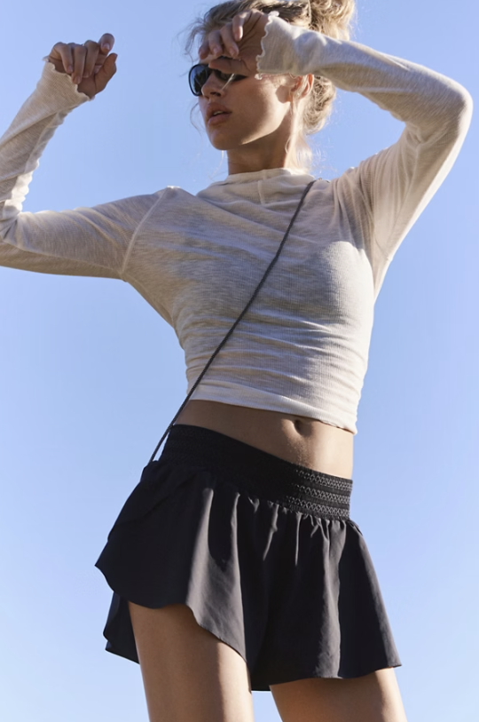 Woman in a white long-sleeve top and black skirt against a clear blue sky.