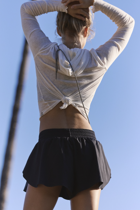 Person wearing a light gray long-sleeve top and black shorts against a clear blue sky.