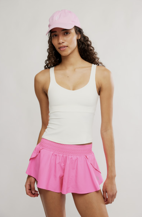 Woman wearing a white tank top and pink skirt with a pink cap on a light gray background