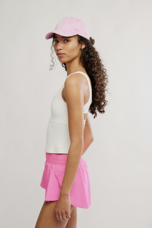 Woman wearing a white tank top, pink skirt, and pink cap on a light gray background
