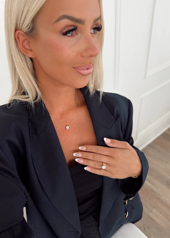 Woman wearing a black blazer with a necklace and ring, indoors.