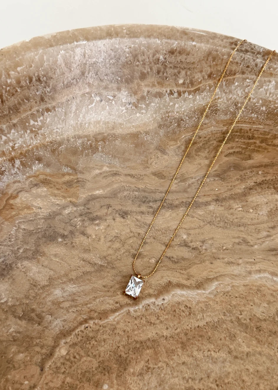 Gold necklace with a diamond pendant on a textured stone surface