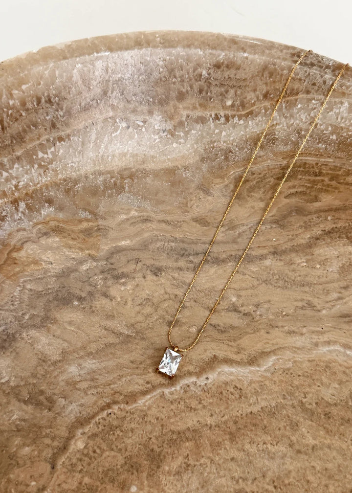 Gold necklace with a diamond pendant on a textured stone surface