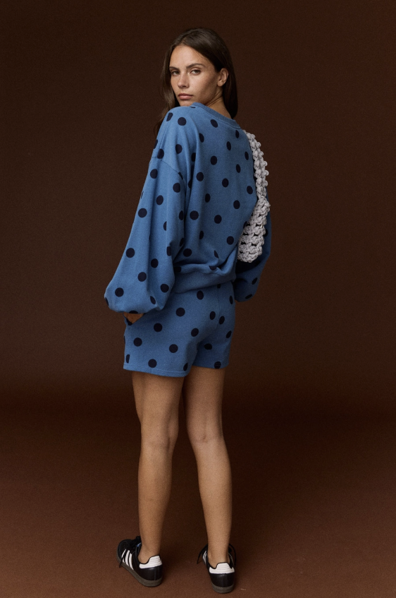 Woman shown from behind wearing blue and black polka dot set on plain background