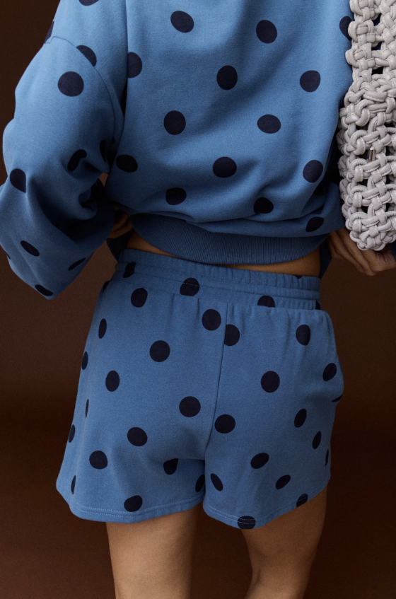 Woman shown from behind wearing blue and black polka dot set on plain background