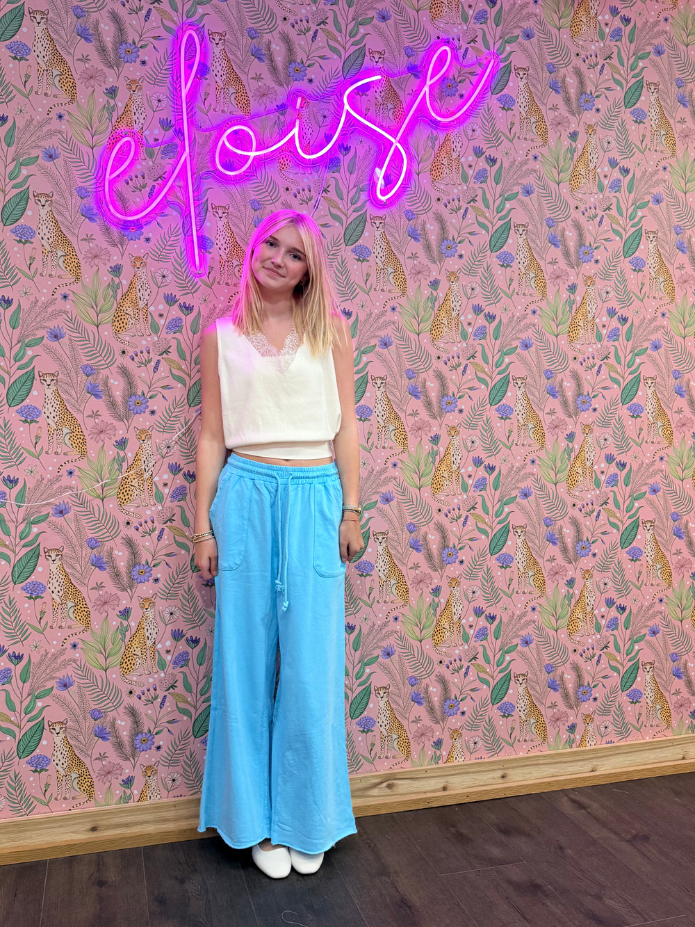Person standing in front of a patterned wall with a neon sign above.