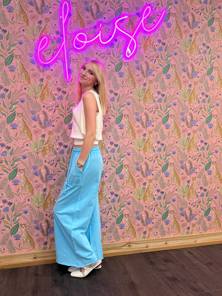 Woman standing in front of a patterned wall with a neon sign above.