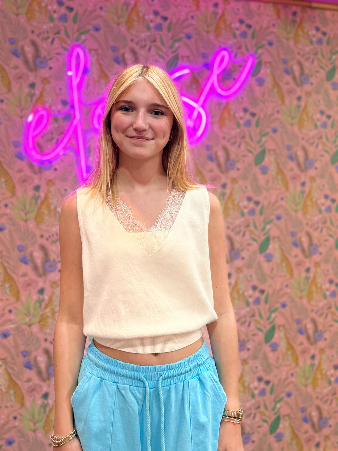 Person wearing a white top and blue pants standing in front of a colorful wall with a neon sign.
