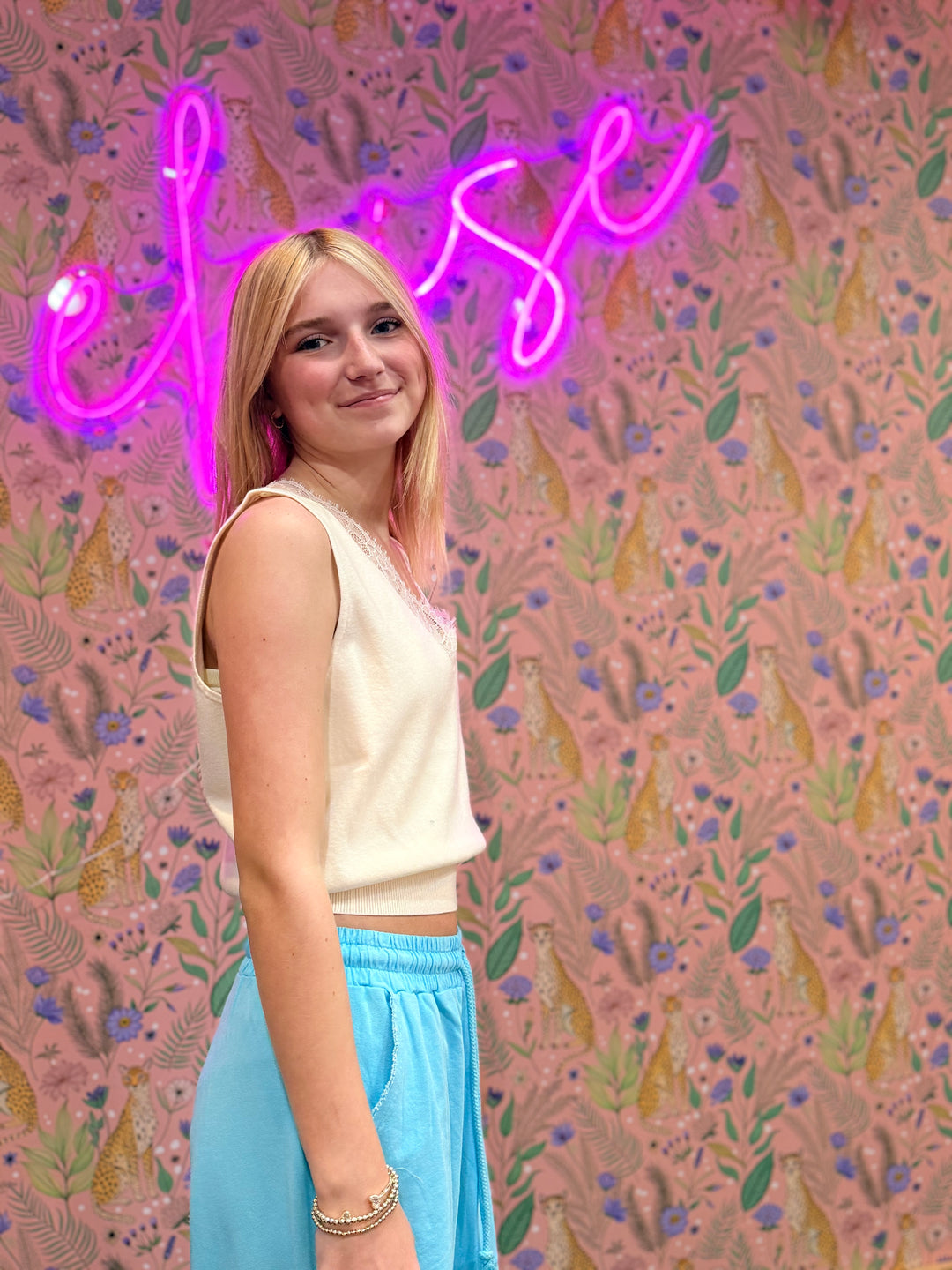 Person standing in front of a colorful wall with floral patterns and a neon sign.