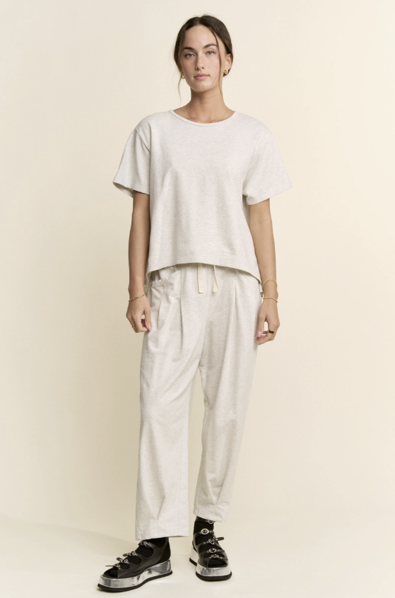 Person wearing a white t-shirt and pants with black shoes on a beige background