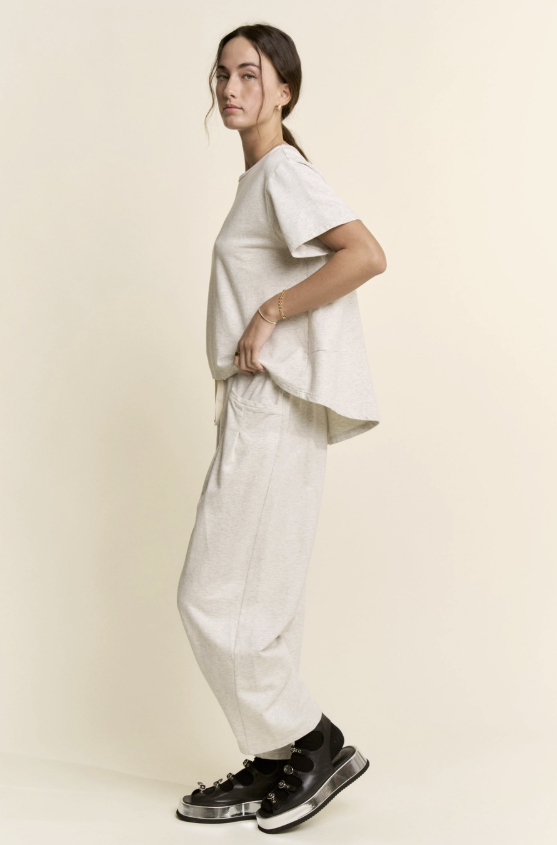 Person wearing a white t-shirt and pants with black shoes on a beige background