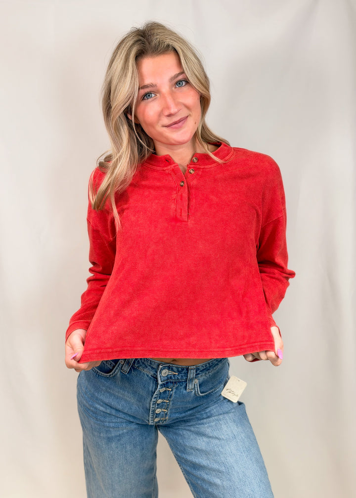 Woman wearing red ribbed henley top with jeans on plain background