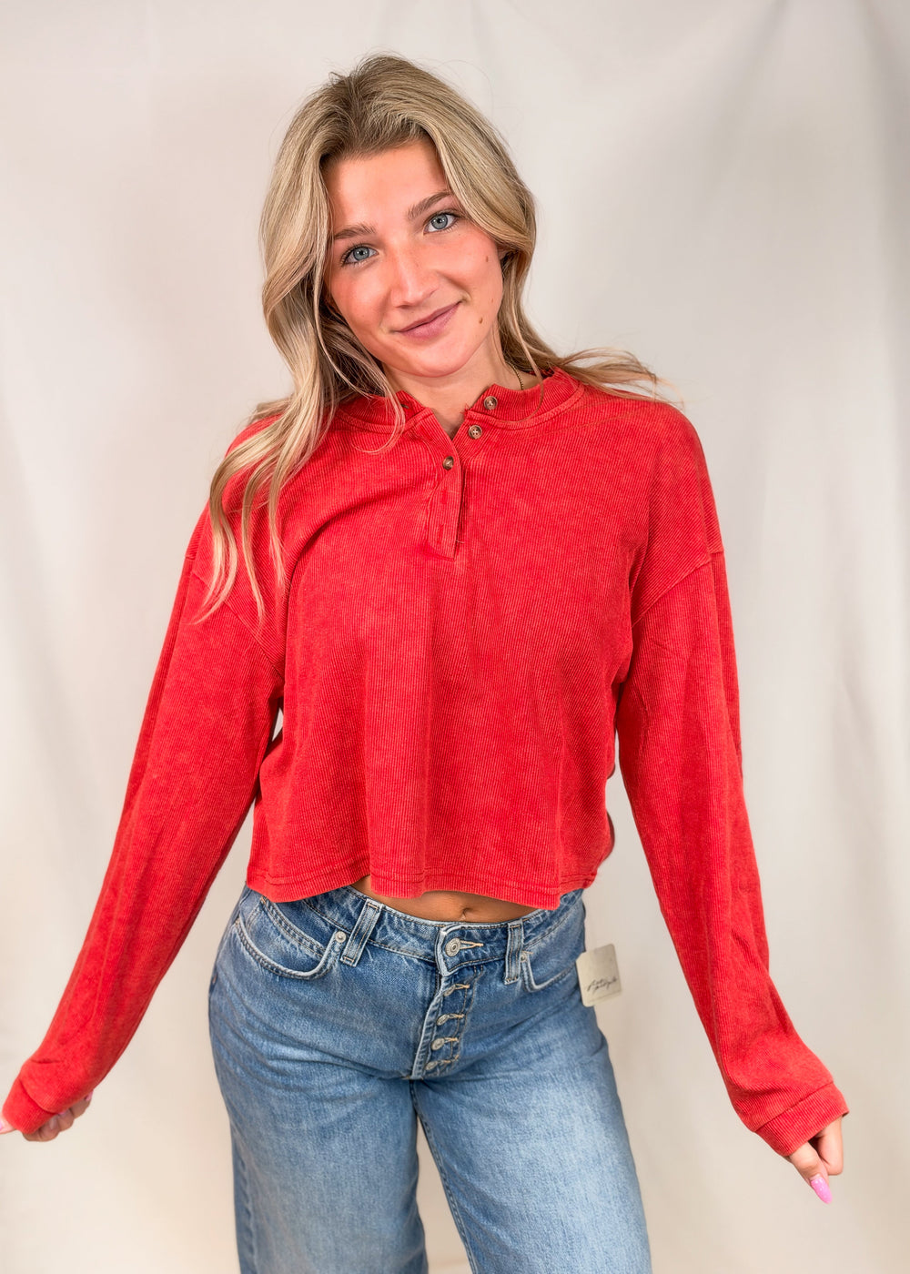 Woman wearing red ribbed henley top with jeans on plain background