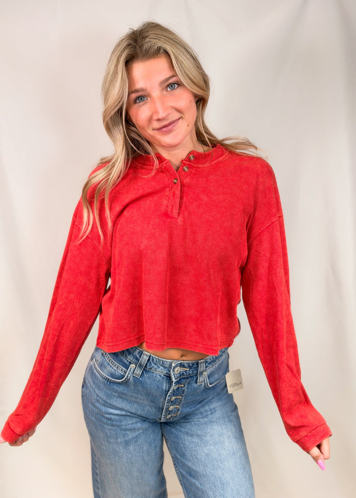 Woman wearing red ribbed henley top with jeans on plain background