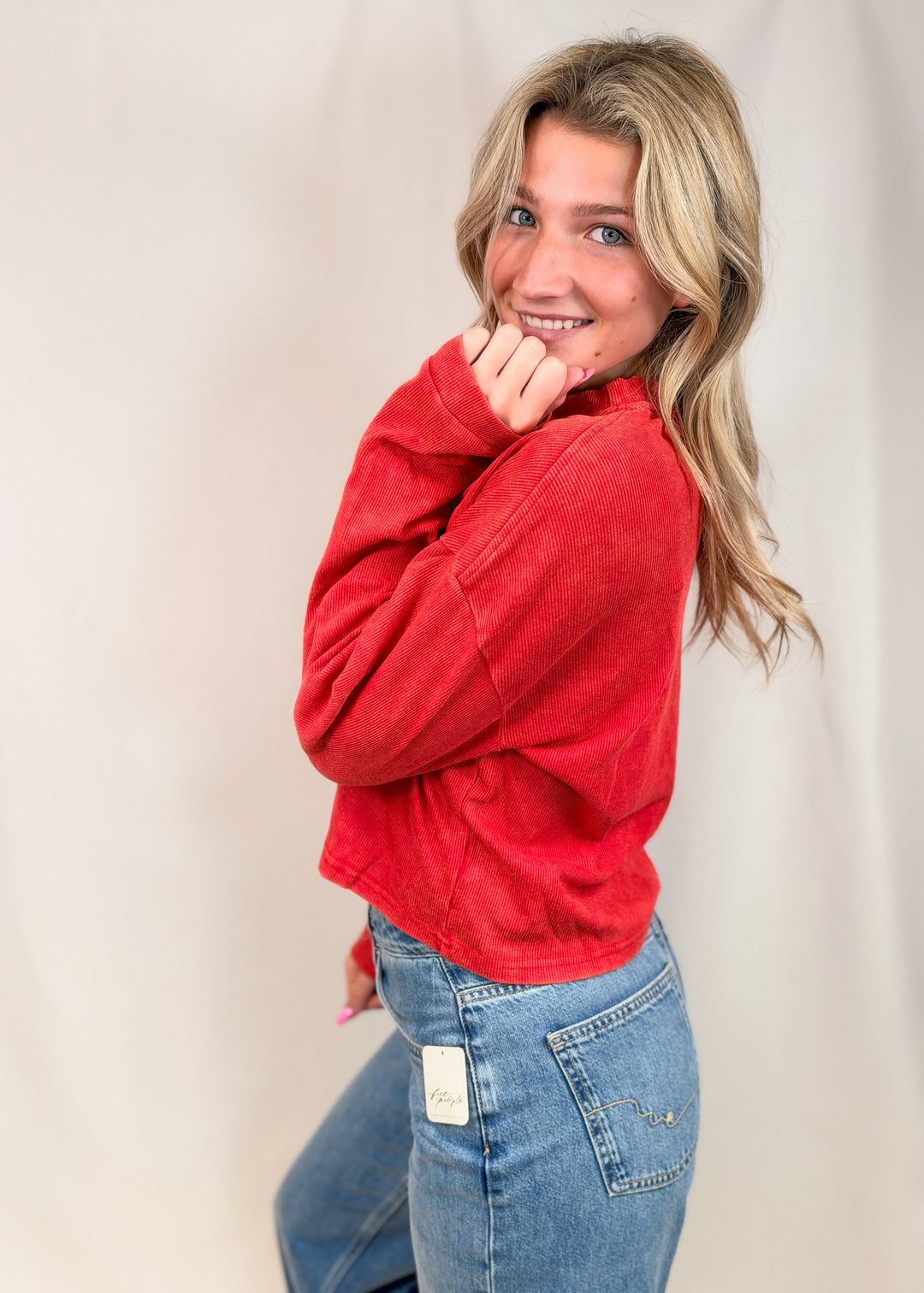 Woman wearing red ribbed henley top with jeans on plain background