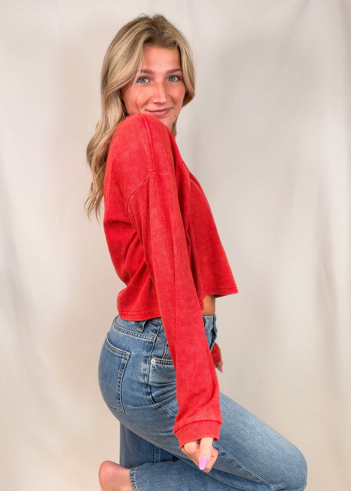 Woman wearing red ribbed henley top with jeans on plain background