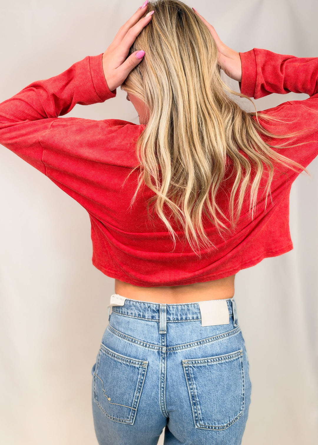 Woman shown from back view wearing red ribbed top with jeans on plain background