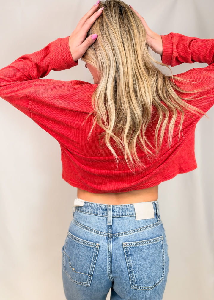 Woman shown from back view wearing red ribbed top with jeans on plain background