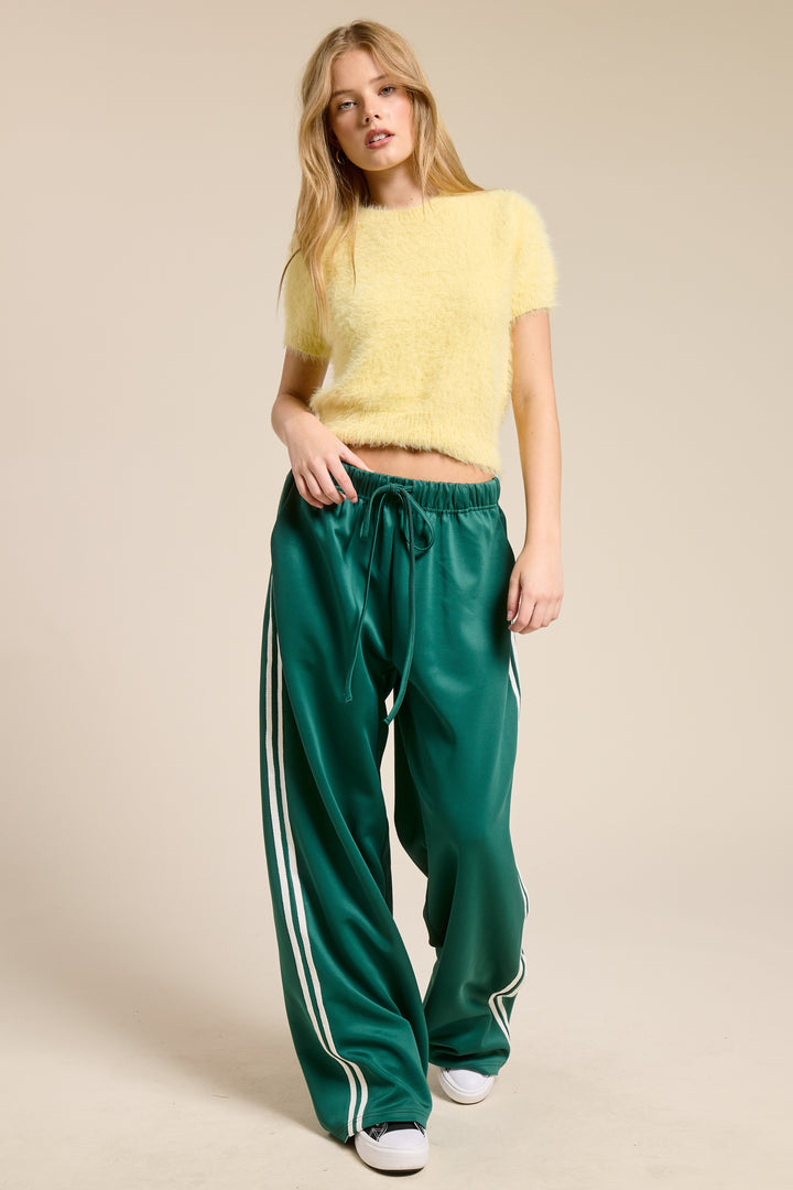 Woman wearing yellow top and green track pants on plain background